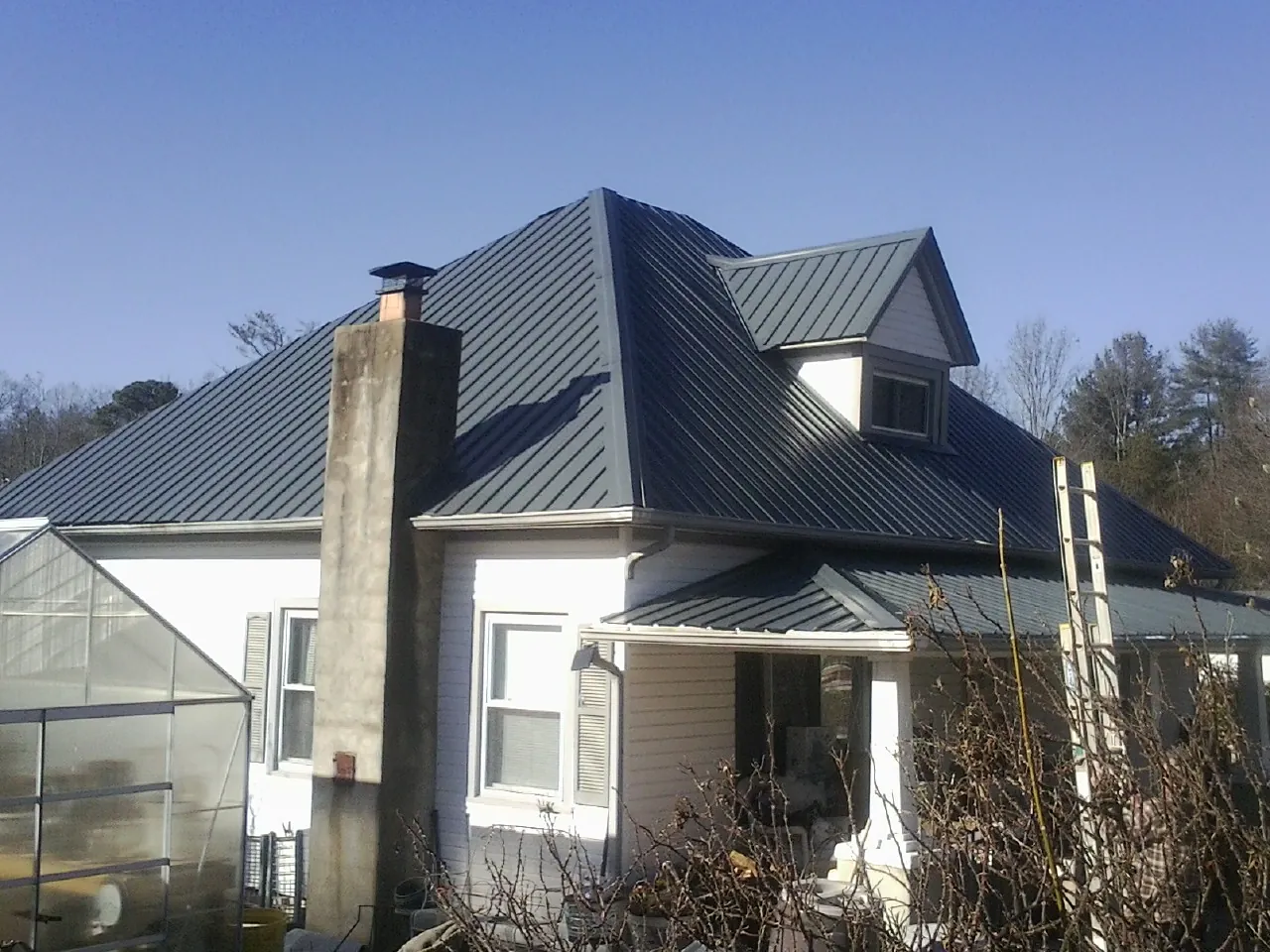 Dark blue standing seam metal roof on a white farmhouse with dormer — Slate & Tile Roof Repair by Roofing Brothers in Larkspur