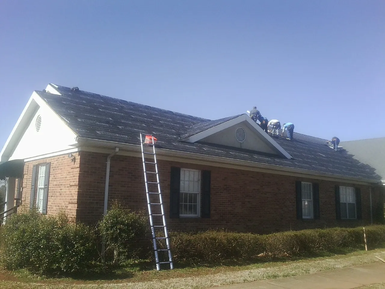 Crew tearing shingles off a brick ranch roof with a ladder set — Emergency Roof Repair work by our crew in Larkspur