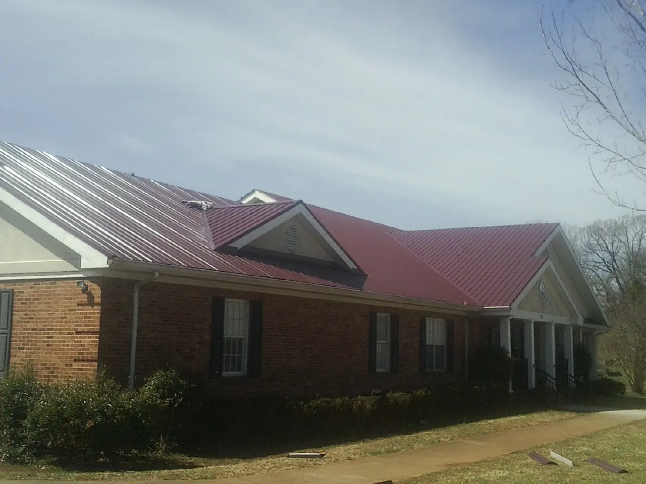 Red metal roof with gabled entries on a long brick building, from a Hail Damage Roof Repair job in Larkspur