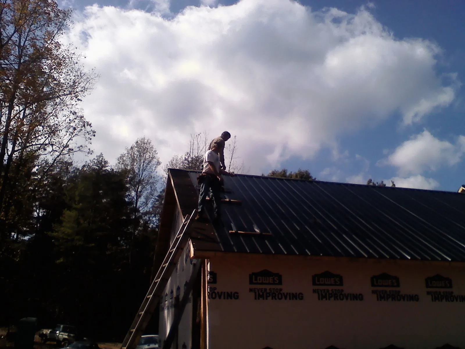 Roofer fastening dark metal panels high against a cloudy sky, from a Roof Inspection job in Larkspur